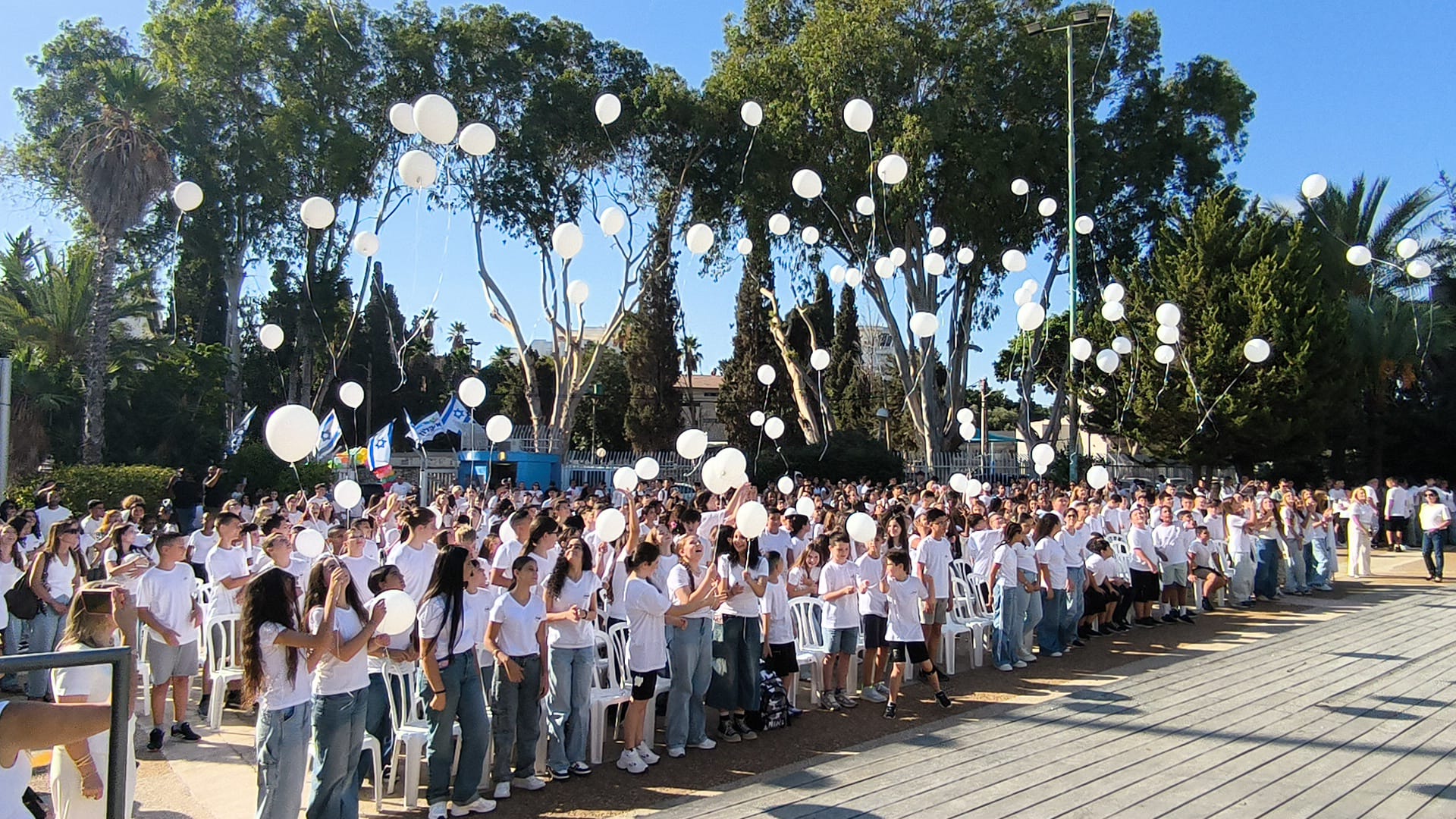 Students and community members gathered outdoors at Afridar Ashkelon as white balloons rise overhead